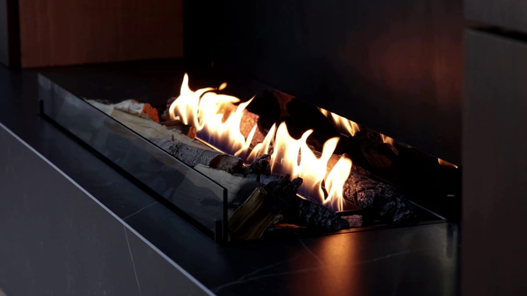 Bioethanol Kamin mit Fernbedienung & App – SmartFire A6 mit Keramikholz in dunkler Naturstein-Wohnwand im modernen Wohnzimmer