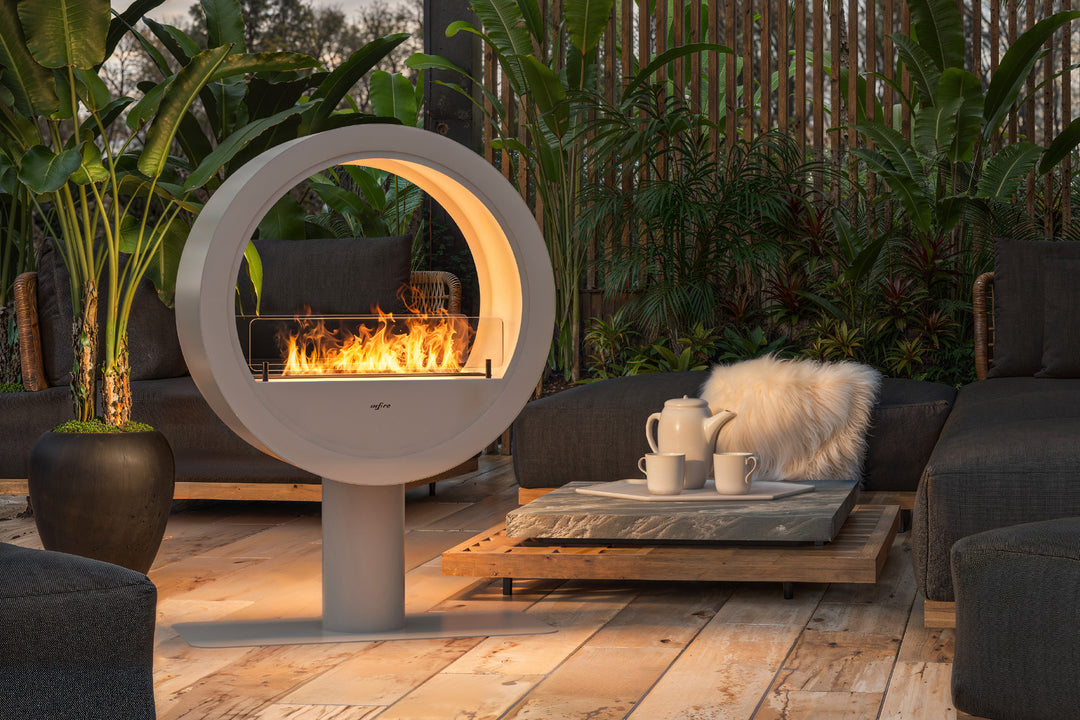 bioethanol-standkamin-ethanolkamin-boden-incycle-2side-infire-weiss-mit-glas-mit-flammen-in-gartenlounge-auf-holzboden-viele-pflanzen