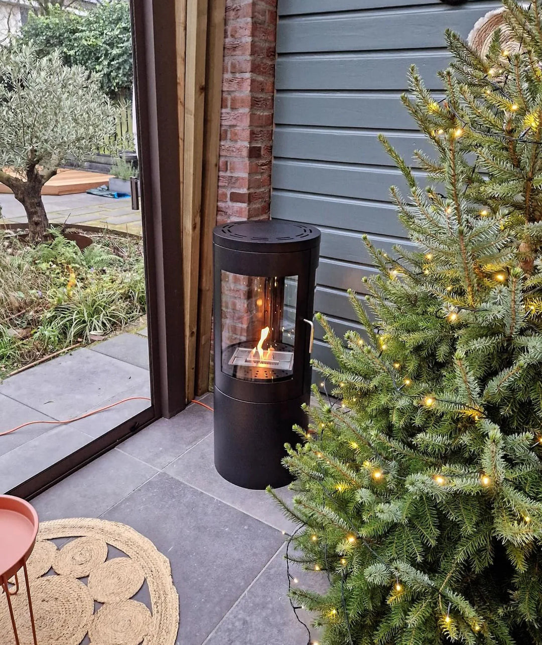 Runder Bioethanol Standkamin Vasto mit Glas in Wohnzimmer / Wintergarten neben Weihnachtsbaum mit Flammenspiel