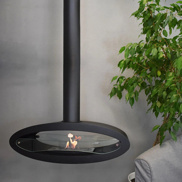 bioethanol-deckenkamin-haengekamin-deckenmontage-decke-ethanolkamin-malema-schwarz-mit-glas-mit-flammen-ellipsenform-frontal-wohnzimmer-vor-grauer-wand-nebensofa-neben-pflanze